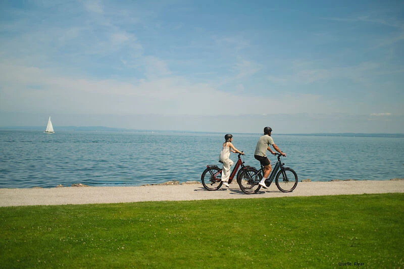 eine-frau-und-ein-mann-fahren-mit-ebikes-am-wasser